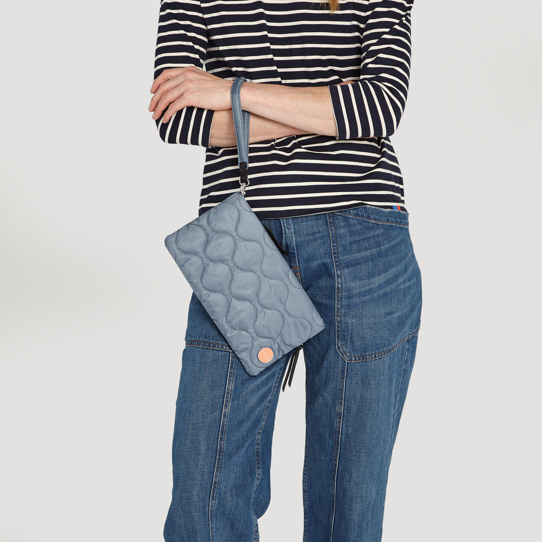shortyLOVE cleo wristlet clutch in steel blue; on model in striped shirt and jeans against white background.