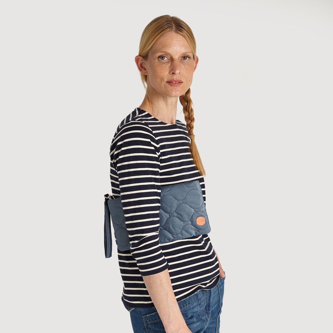 shortyLOVE cleo wristlet clutch in steel blue; on model in striped shirt and jeans against white background.