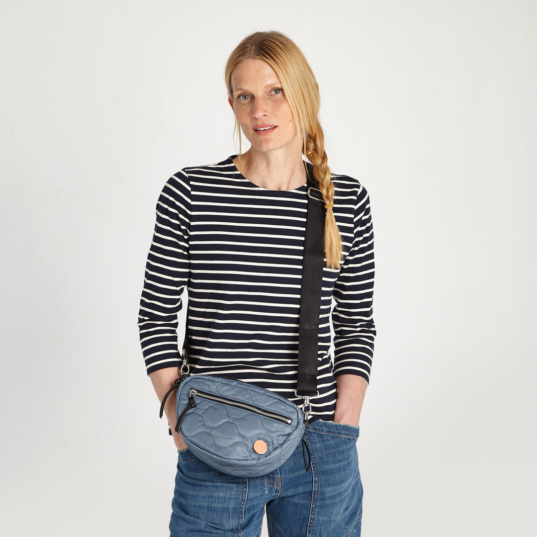 shortyLOVE small cruiser small crossbody bag in steel blue; on model in striped shirt and jeans against white background.