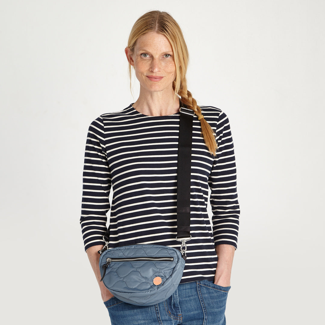 shortyLOVE small cruiser small crossbody bag in steel blue; on model in striped shirt and jeans against white background.