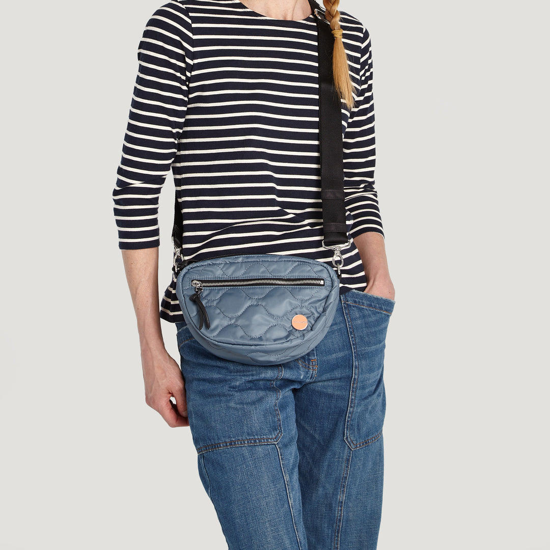 shortyLOVE small cruiser small crossbody bag in steel blue; on model in striped shirt and jeans against white background.