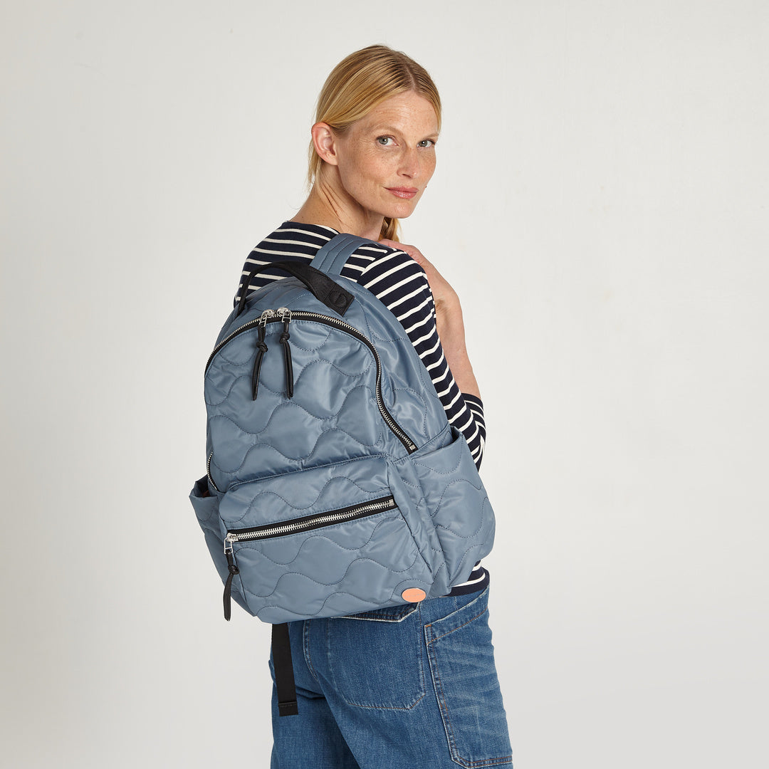 shortyLOVE tate backpack in steel blue; on model in striped shirt and jeans against white background.