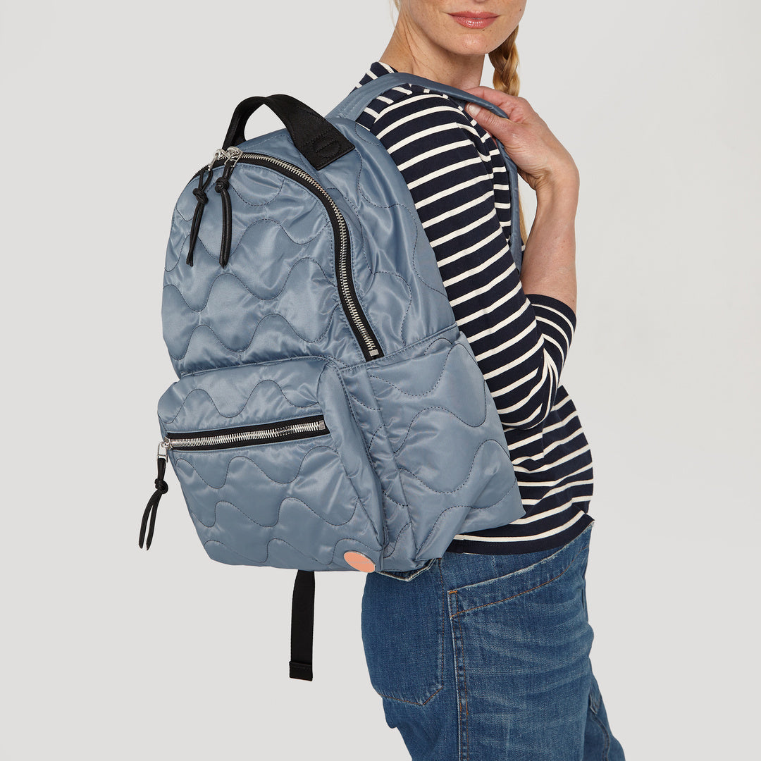 shortyLOVE tate backpack in steel blue; on model in striped shirt and jeans against white background.