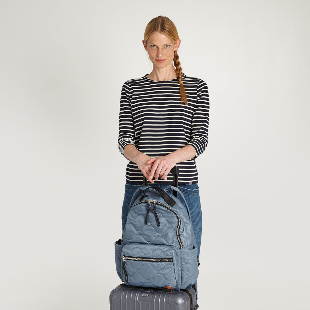 shortyLOVE tate backpack in steel blue; on luggage with model in striped shirt and jeans against white background.