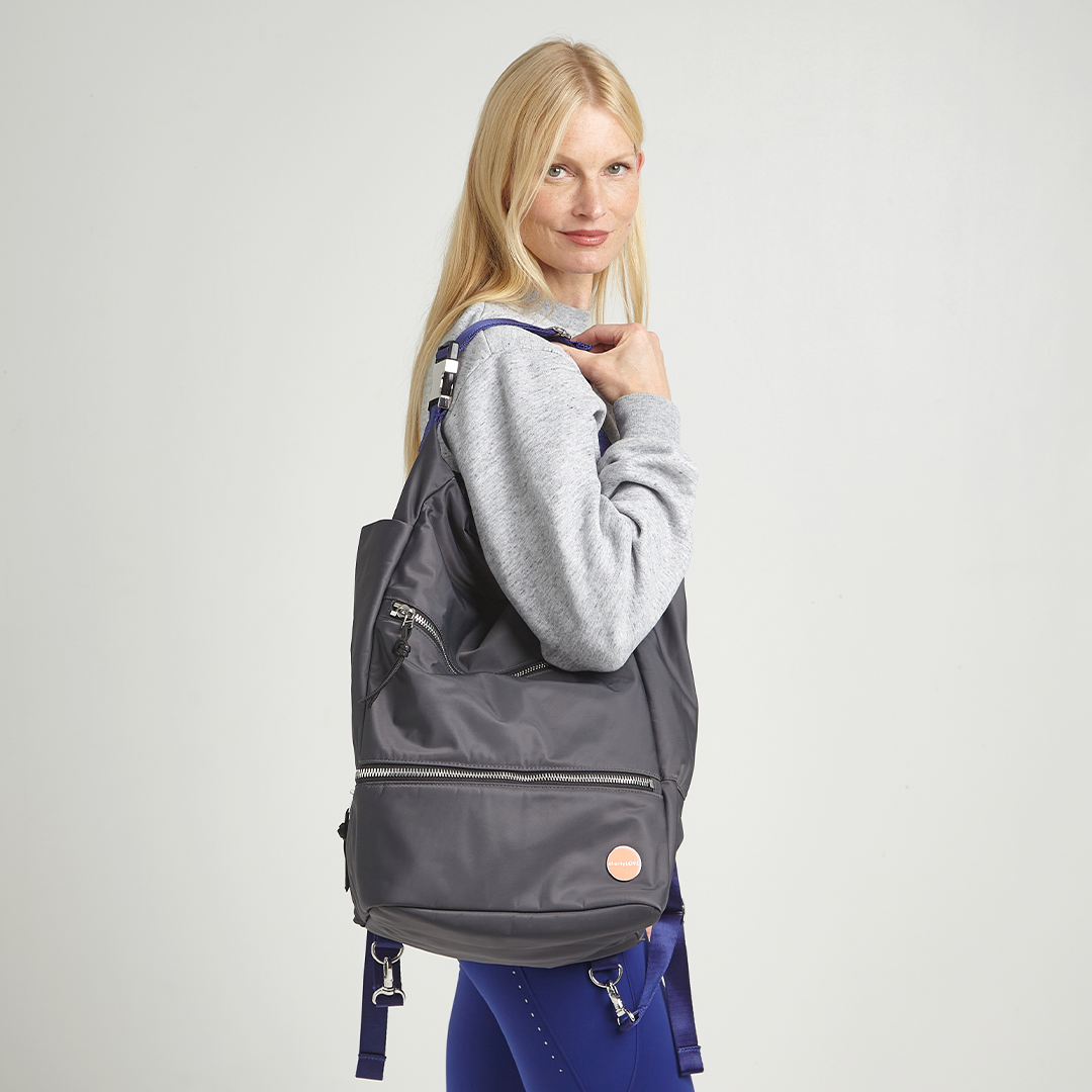 Woman holding a charcoal backpack against a plain background
