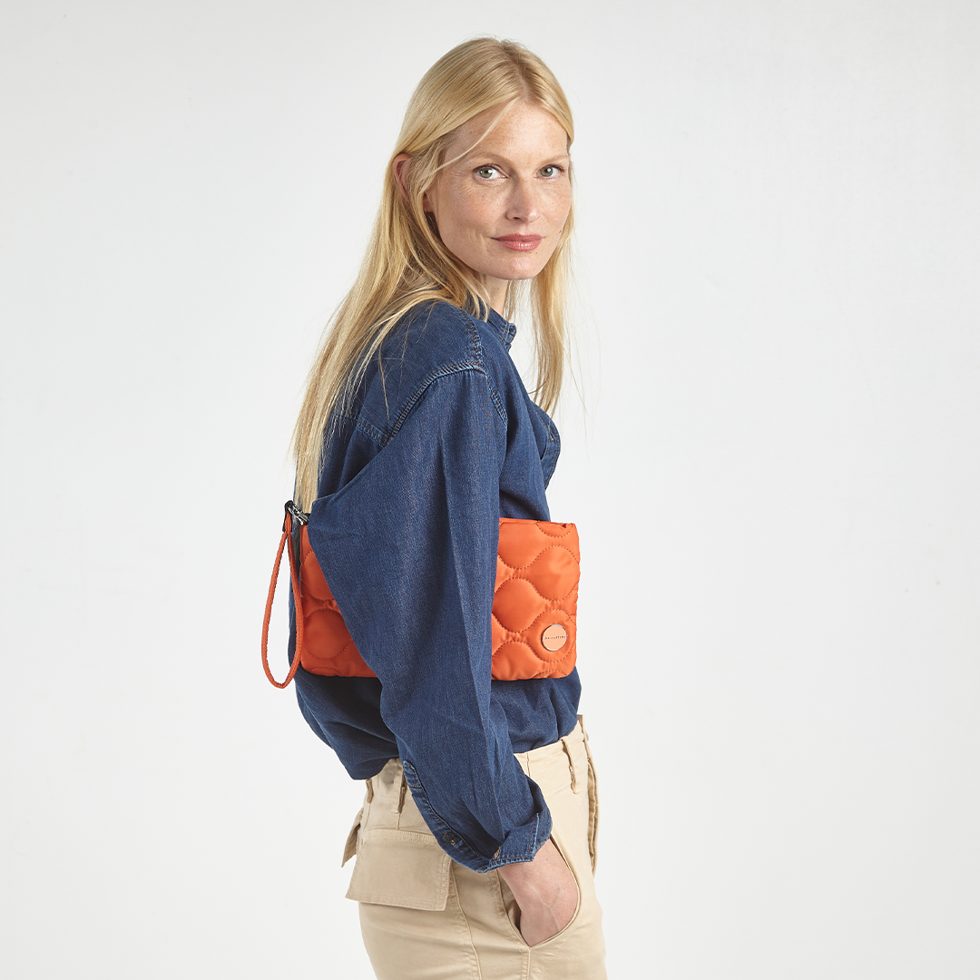 woman holding an orange cleo clutch under her arm against a white background