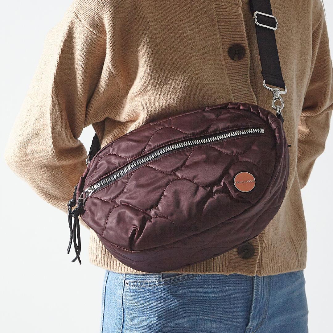 Person wearing a bordeaux quilted cruiser bag over one shoulder against a neutral background