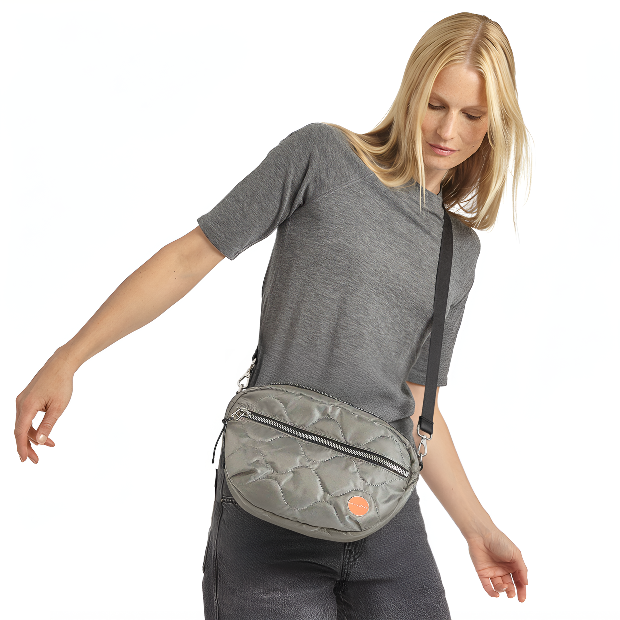 Woman wearing a gray quilted cruiser crossbody bag on a white background