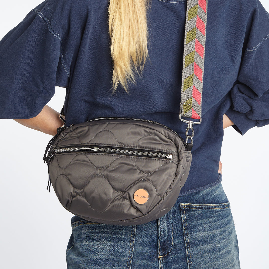 Person wearing a pewter quilted cruiser crossbody bag with a colorful strap on a white background