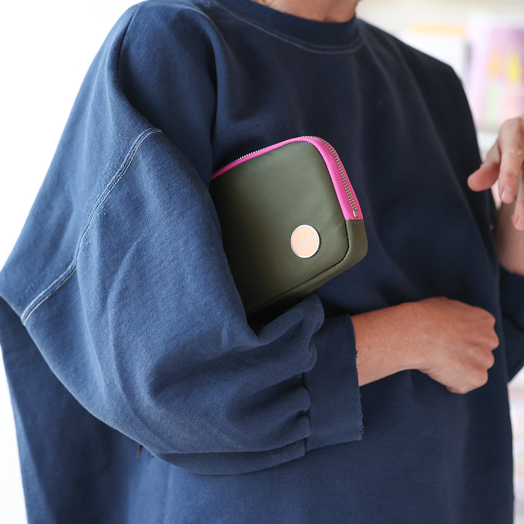 Person wearing a navy blue sweatshirt with an army green and pink jetty wallet/clutch under her arm