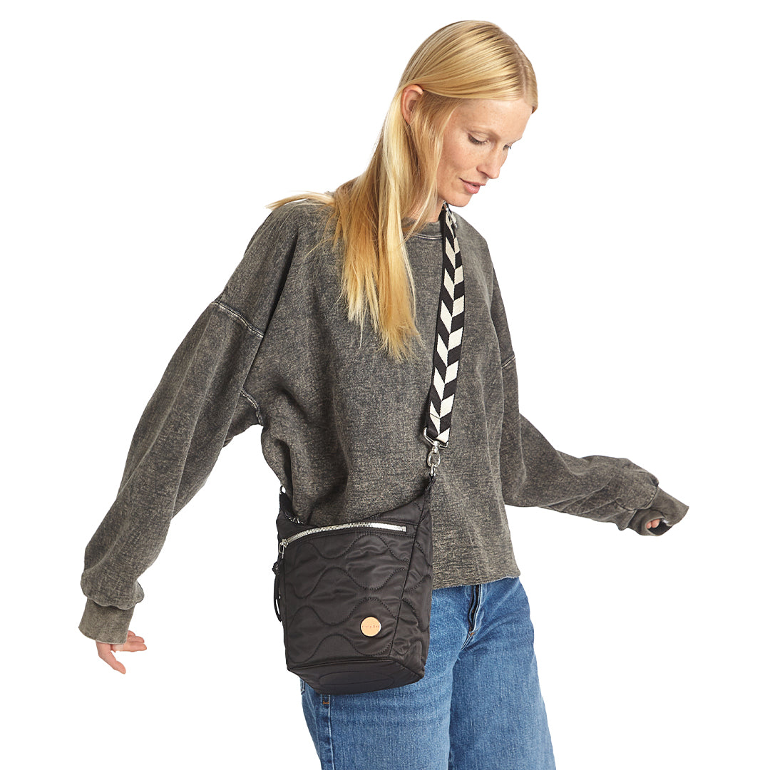 Woman wearing a black marcel quilted crossbody bag with a white and black striped strap on a white background