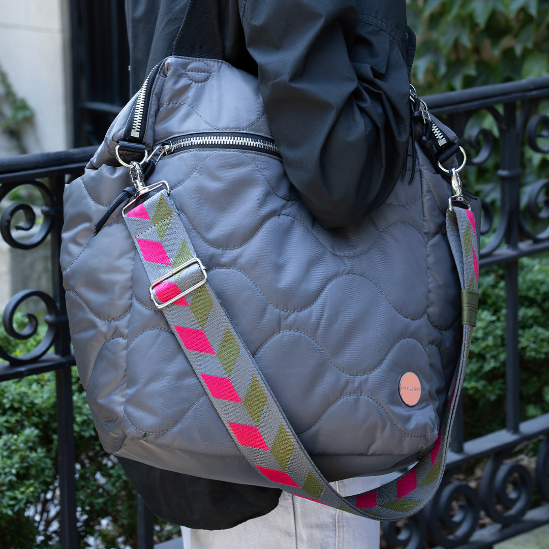 Pewter gray quilted bag with a colorful strap held by a person outdoors.