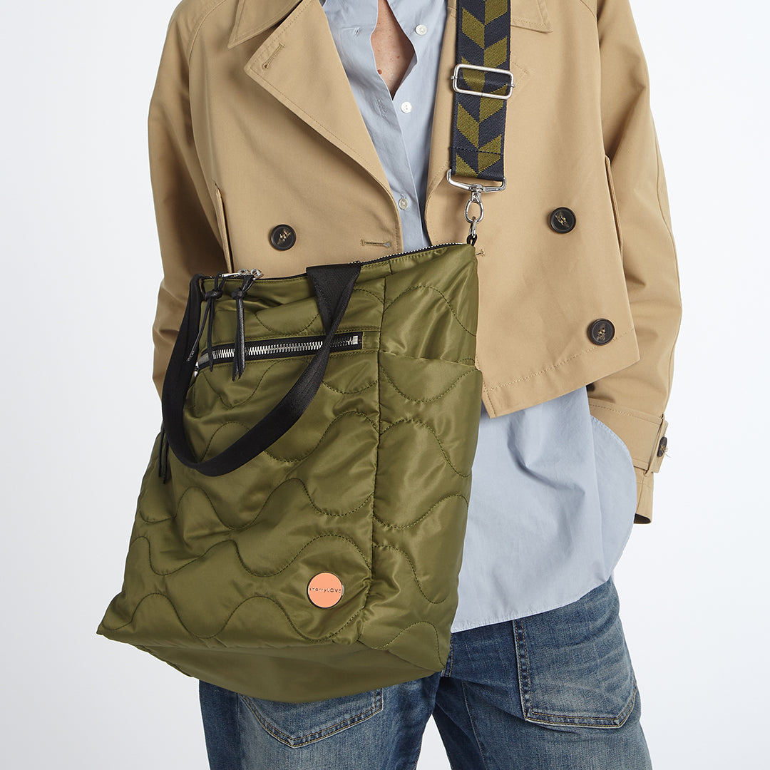 Person wearing a beige coat with a sage green quilted ranger tote bag over their shoulder on a white background