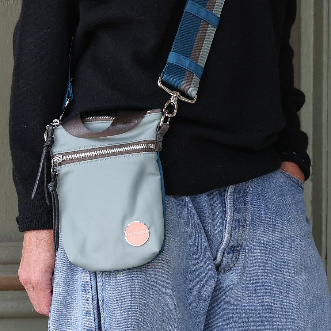Person wearing a slate/teal shorthand crossbody bag with a strap over their shoulder.