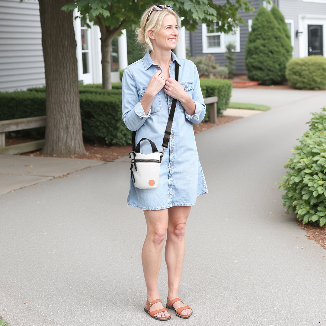 Woman in a denim dress with a white shorthand crossbody bag walking on a sidewalk.