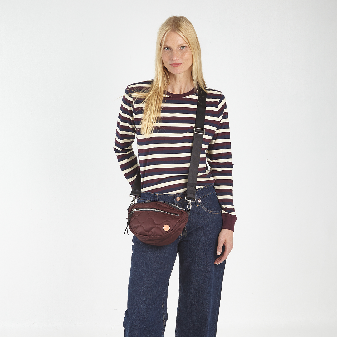 Woman wearing a striped shirt and suspenders with a Bordeaux quilted crossbody bag on a white background
