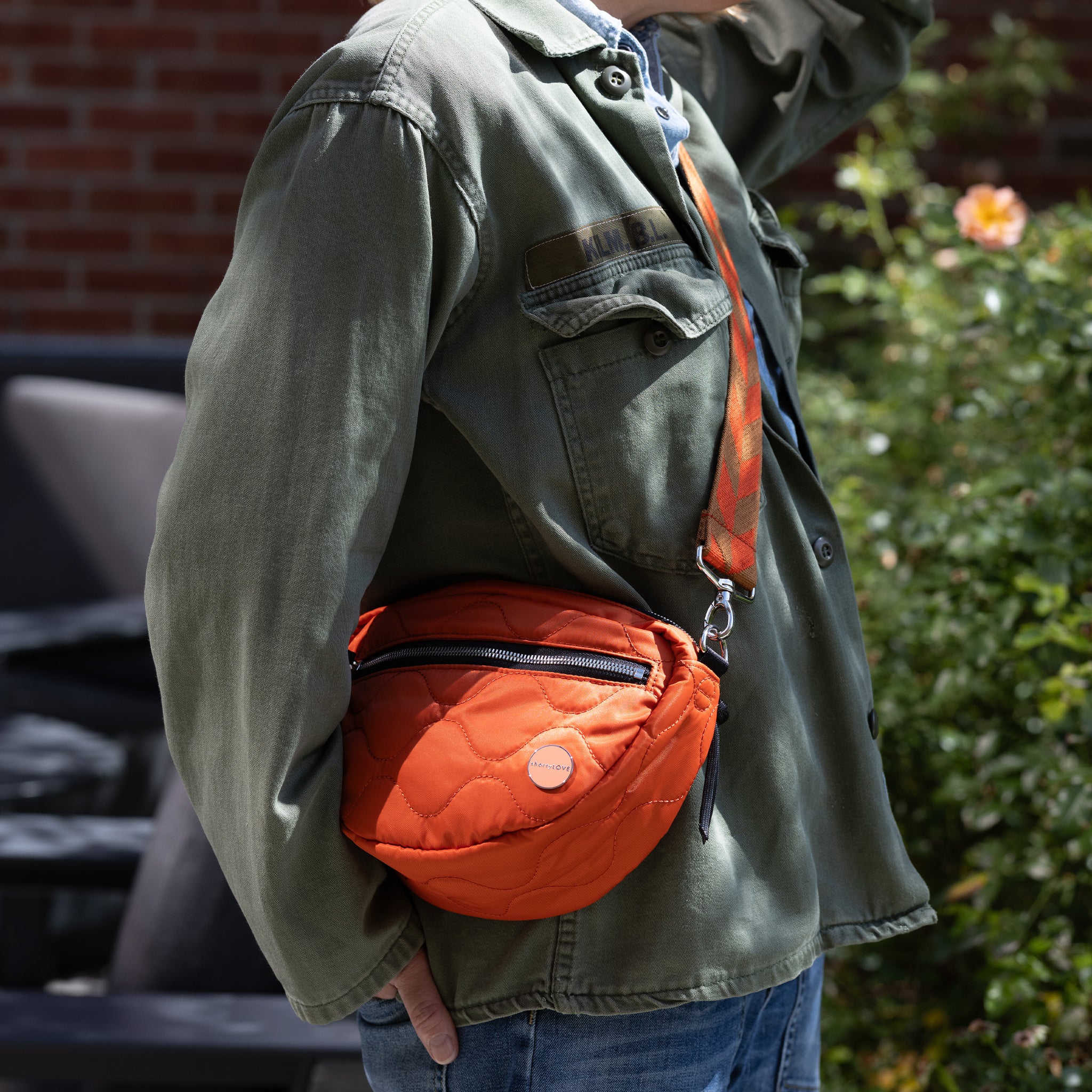 Person wearing an orange quilted crossbody bag with a green jacket outdoors.