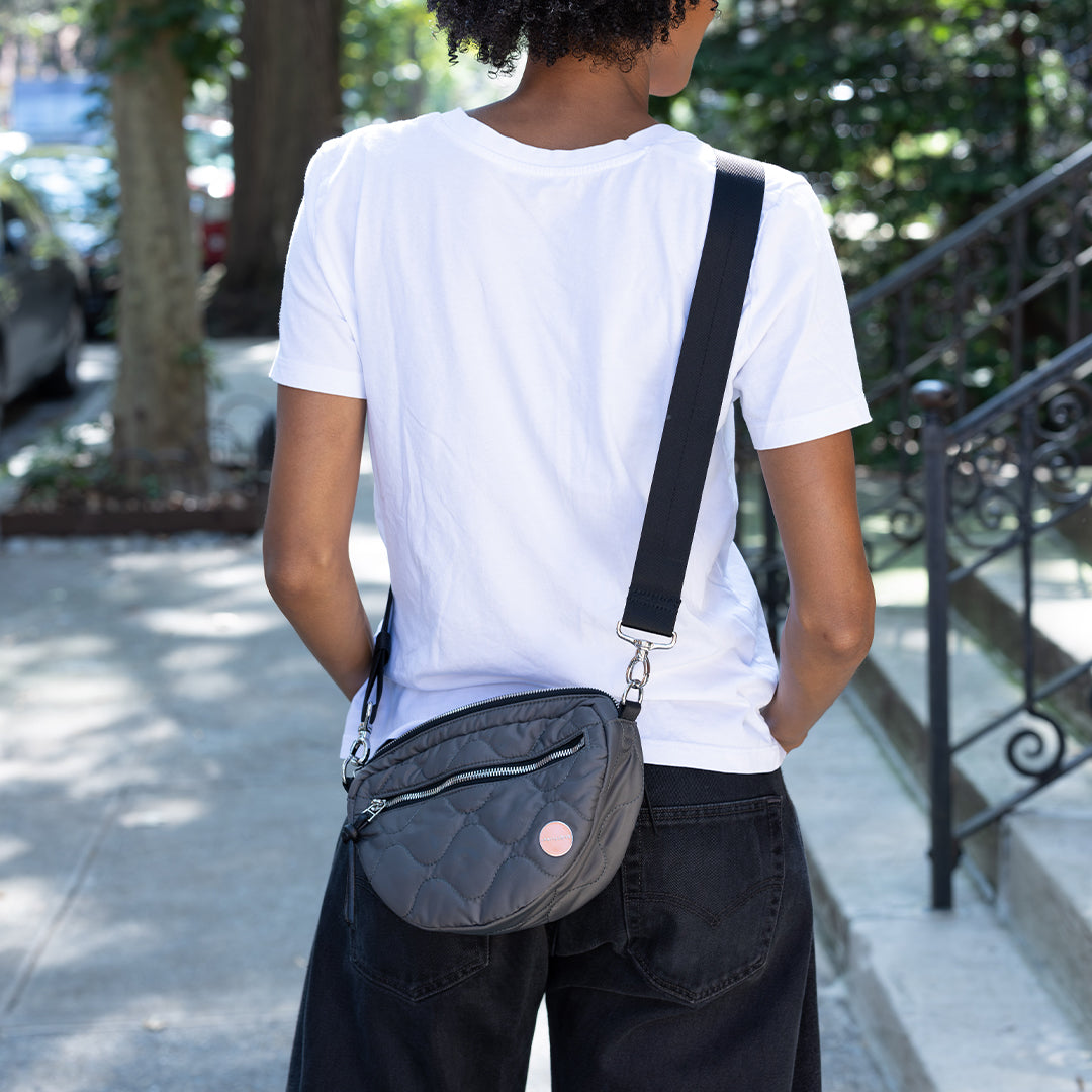 Person wearing a white t-shirt and black pants with apewter small cruiser crossbody bag on a sidewalk.