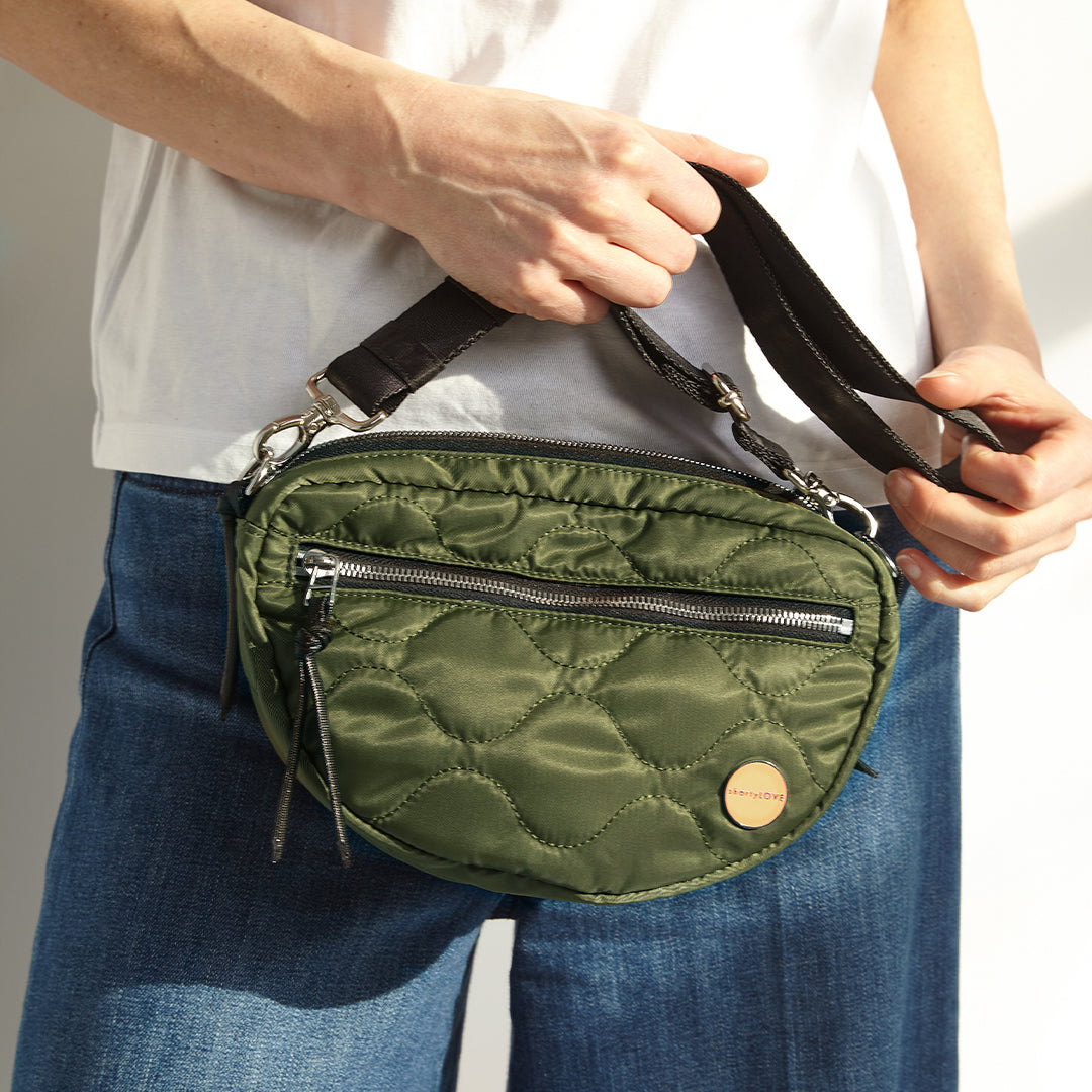 Person holding a sage quilted small cruiser crossbody bag with a visible brand logo.