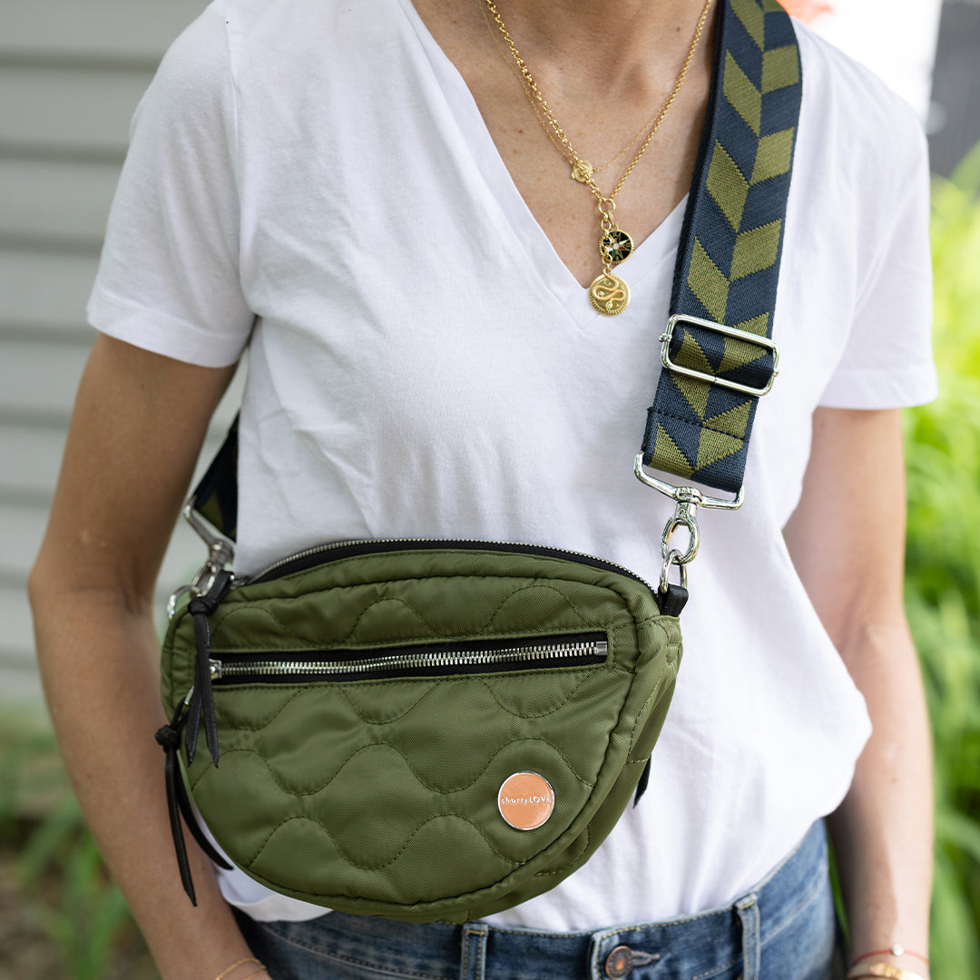 Woman wearing a sage green cruiser quilted crossbody bag with a colorful crossbody strap on a white background
