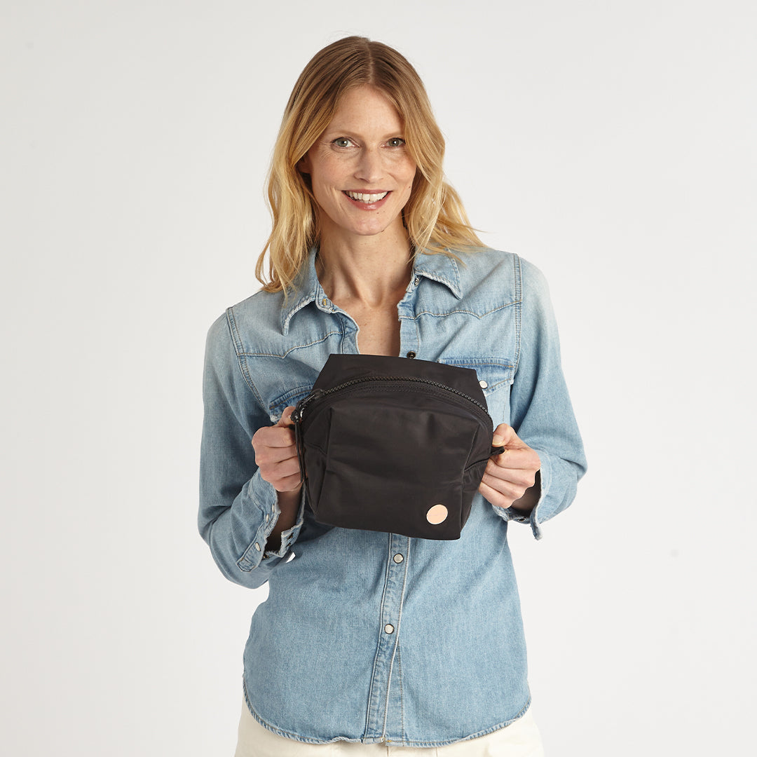 Woman holding a black cosmetic bag against a plain background