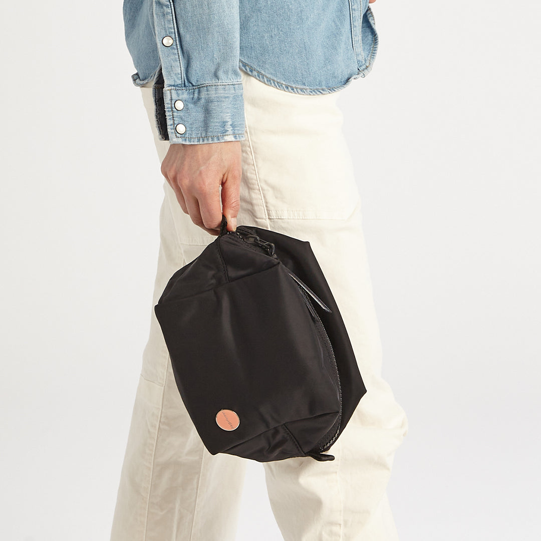 Person holding a black cosmetic bag with a visible brand logo on a white background
