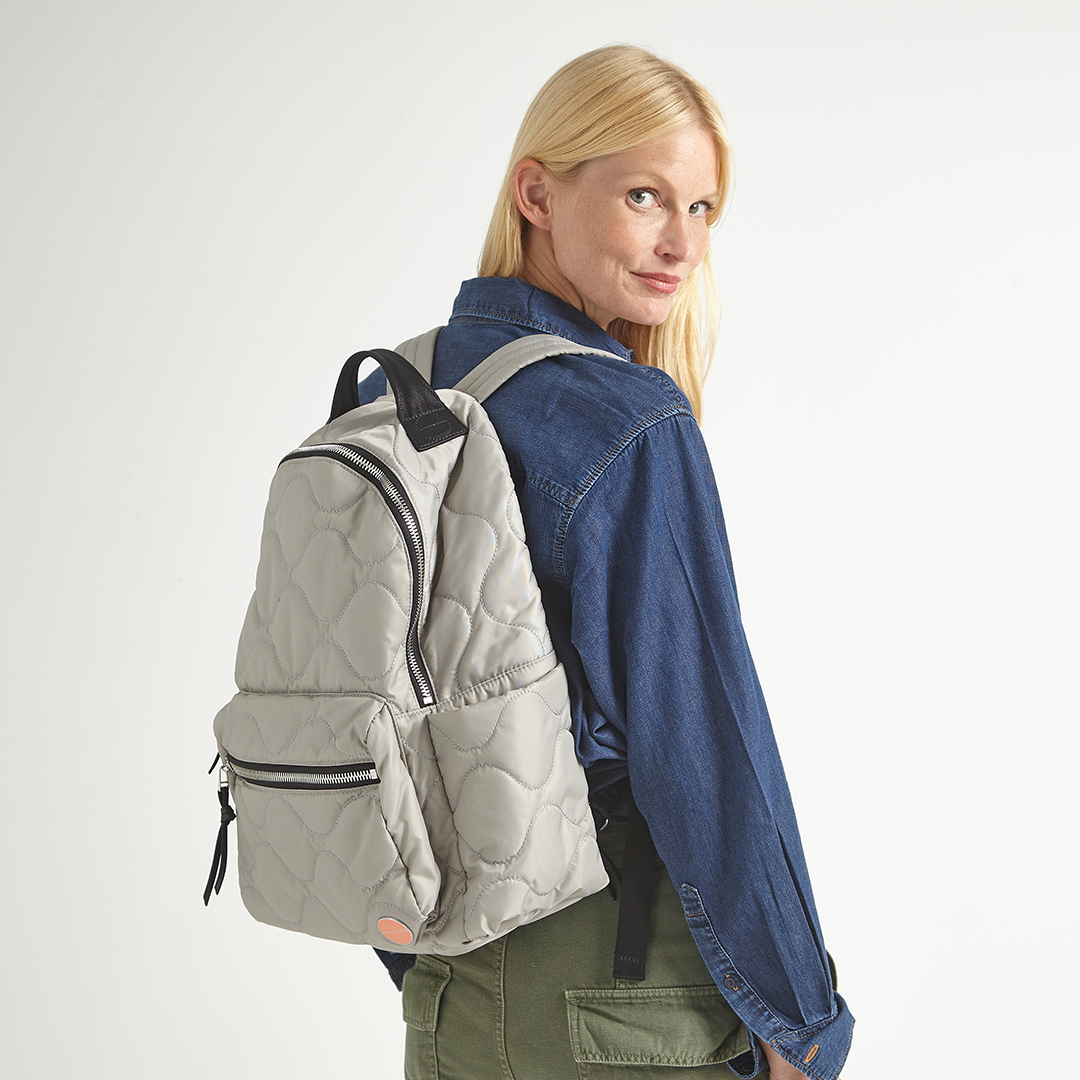 Woman wearing a gray quilted tate backpack on a plain background