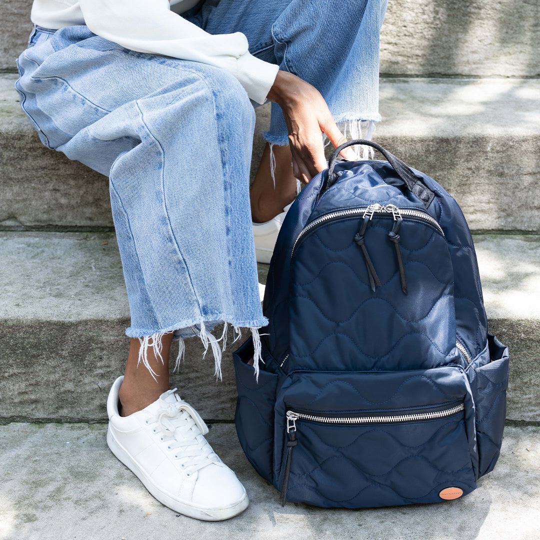 Person sitting on steps with a midnight blue quilted tate backpack