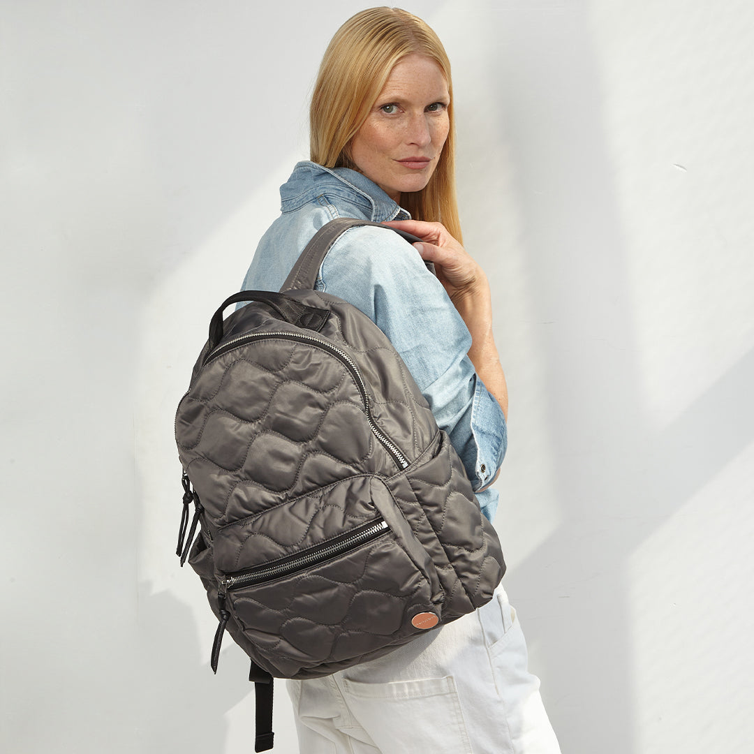 woman wearing a pewter tate quilted backpack against a plain background