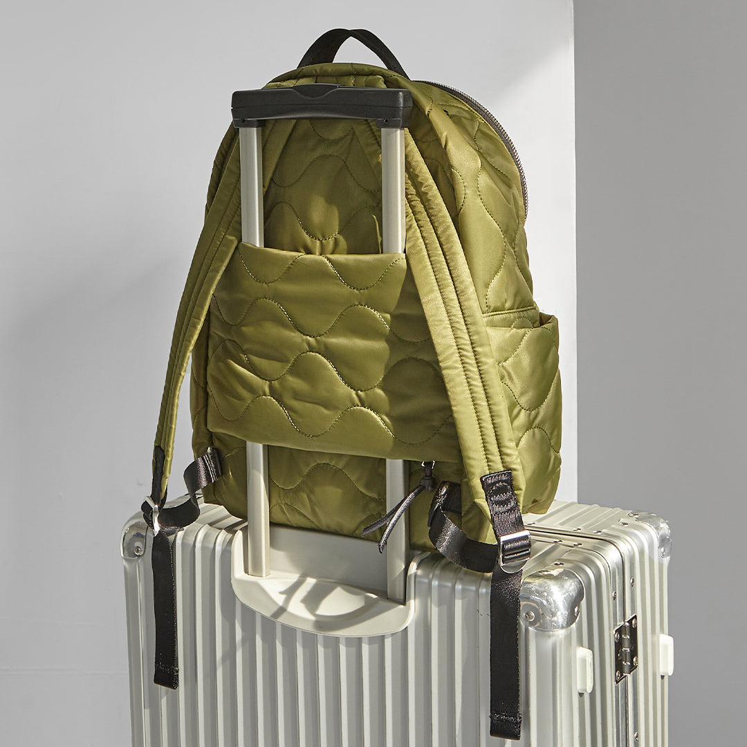 Sage Green quilted tate backpack with a rolling suitcase on a light gray background