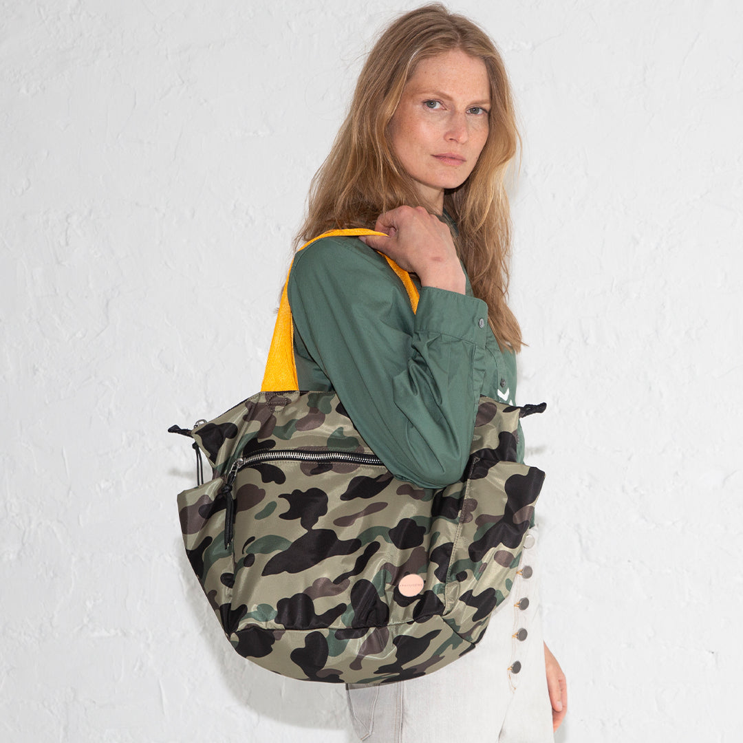 Woman holding a camouflage tillie tote bag against a white background