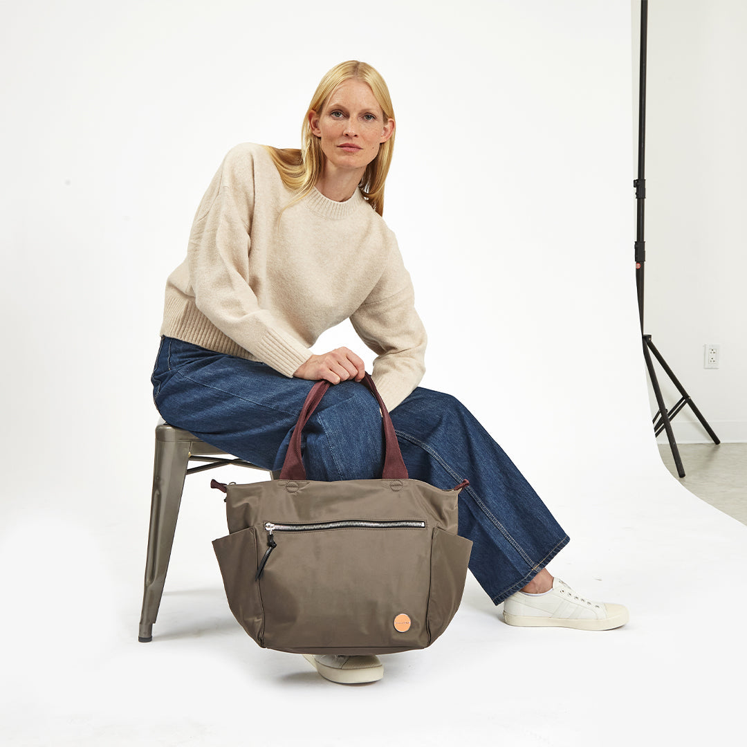 Woman sitting on a chair holding a mocha tillie tote bag against a white background