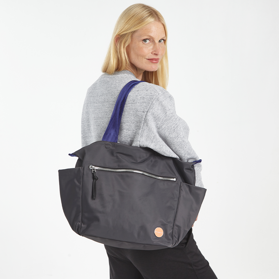 Woman carrying a charcoal gray tillie tote bag with a blue strap on a white background