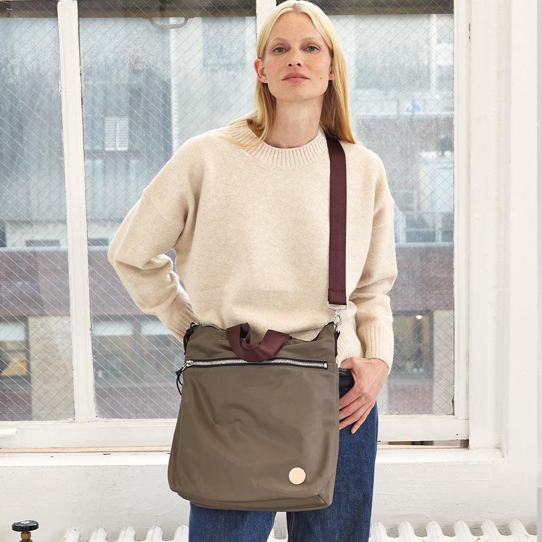 Woman holding a mocha wonder crossbody shoulder bag in front of a window