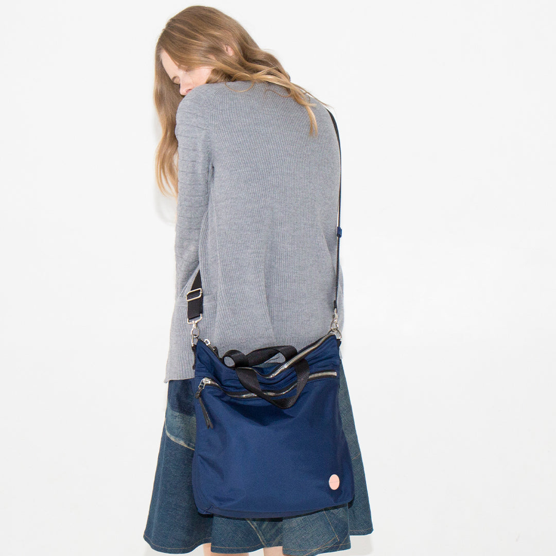 Person wearing a navy wonder crossbody bag over their shoulder on a white background