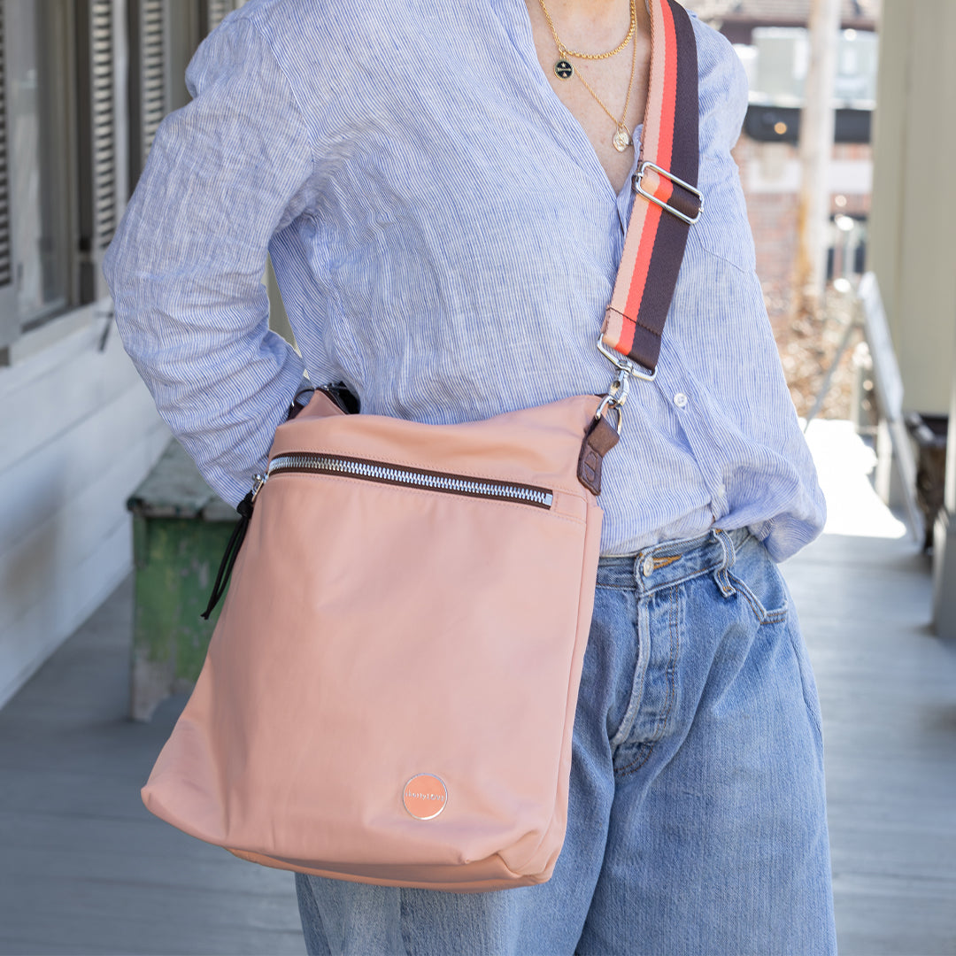 Person holding a dusty peach crossbody bag with a blurred background