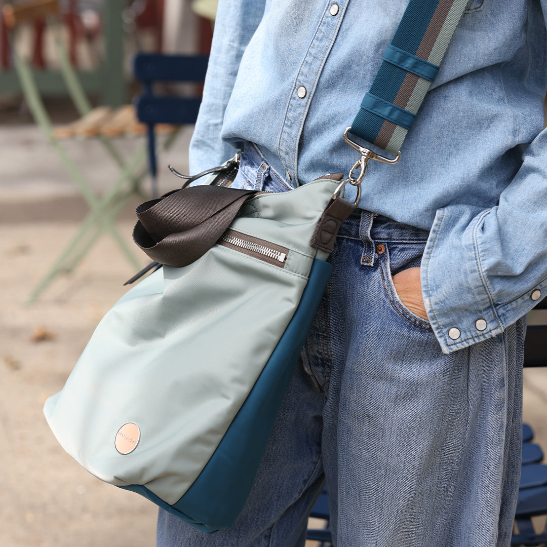 Person wearing a lslate/teal wonder crossbody bag on a blurred outdoor background