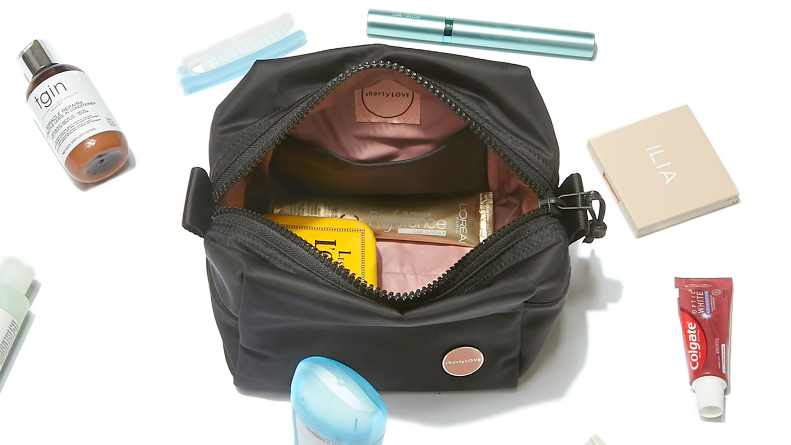 shortyLOVE stevie cosmetic bag in black; top is open to show blush lining and several cosmetic items; several other cosmetic items encircle the bag against a white background.