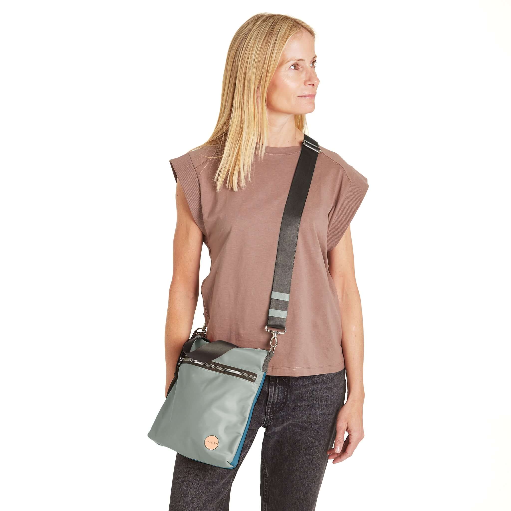 shortyLOVE amuse medium sized crossbody bag in slate/teal; on model in blush rose top and jeans against white background.