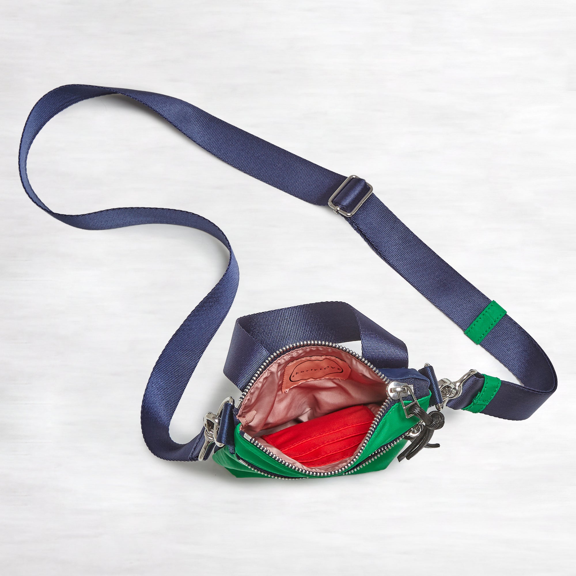 shortyLOVE shorthand small crossbody bag in grass green/navy; top-down view showing interior blush/red lining against white background.