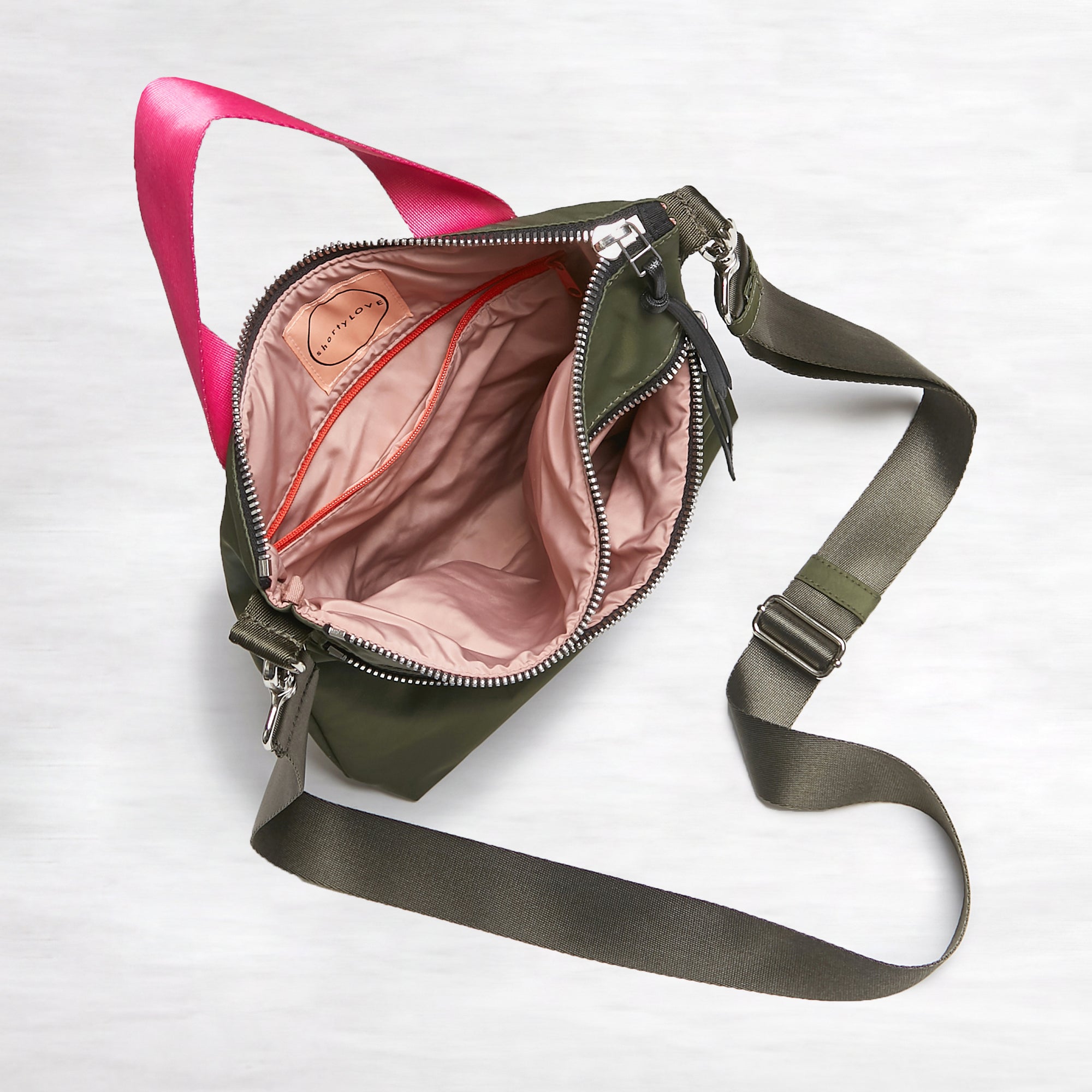 shortyLOVE amuse medium sized crossbody bag in army green; top-down view showing interior pink lining against white background.
