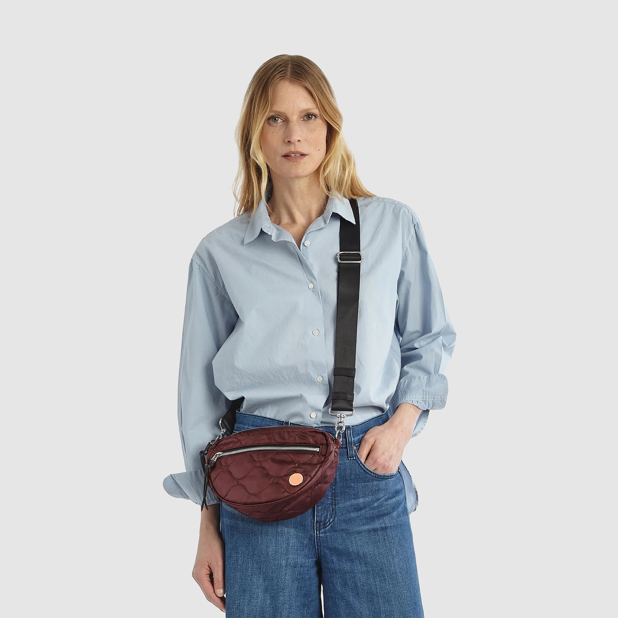 Model in blue top and jeans wearing a bordeaux small cruiser crossbody bag.