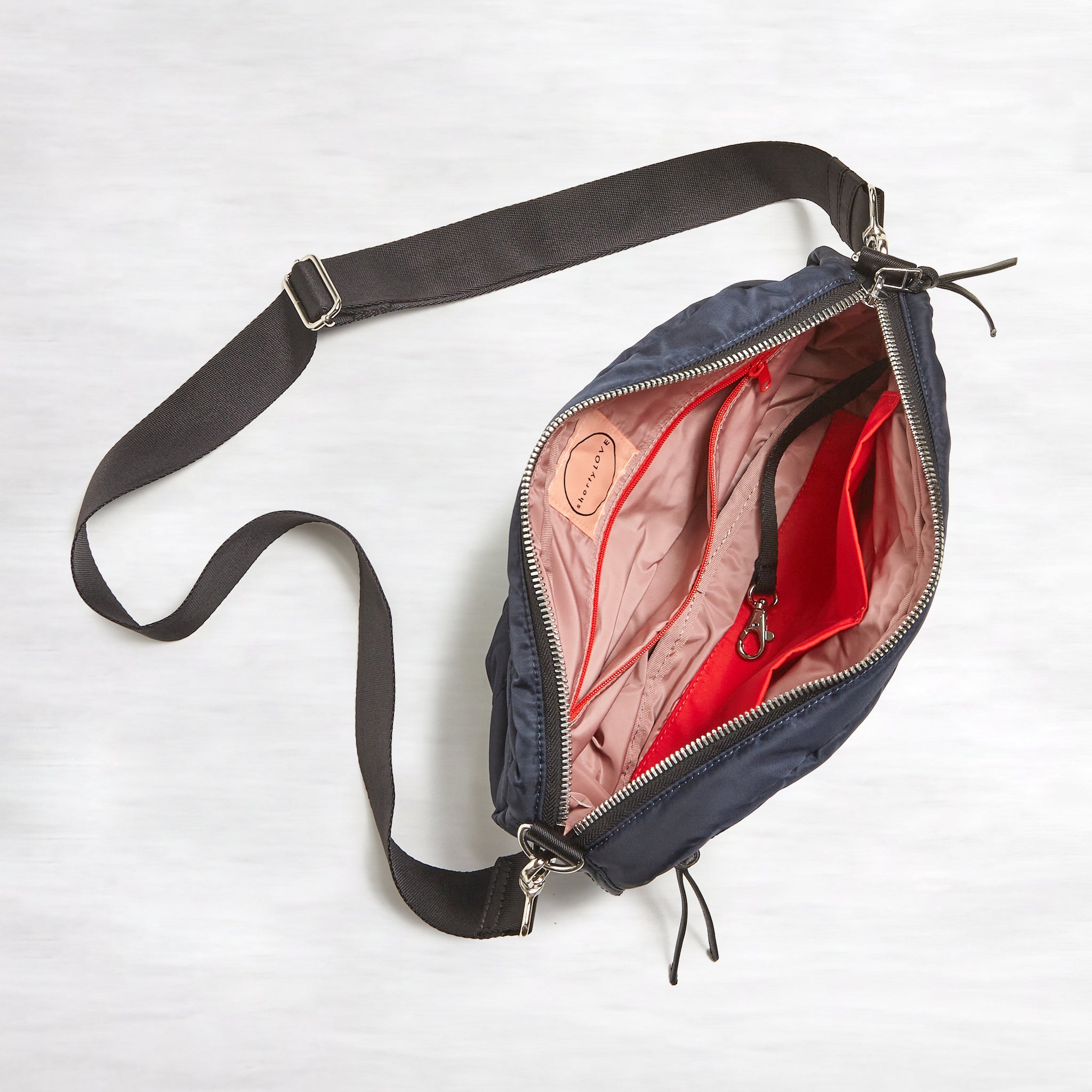 shortyLOVE cruiser medium crossbody bag in midnight; top-down view showing interior blush lining against white background.