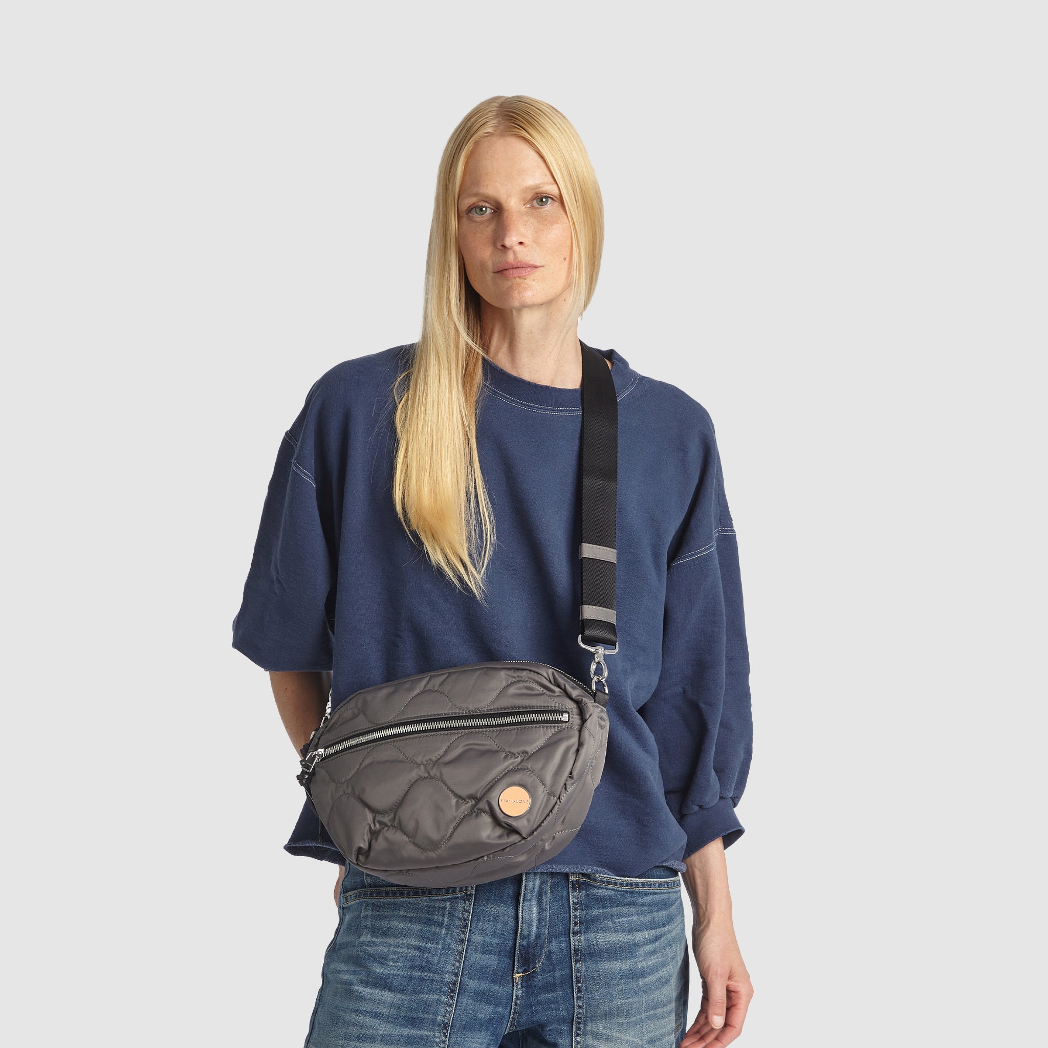 Person wearing a blue oversized shirt and jeans with a pewter quilted cruiser crossbody bag
