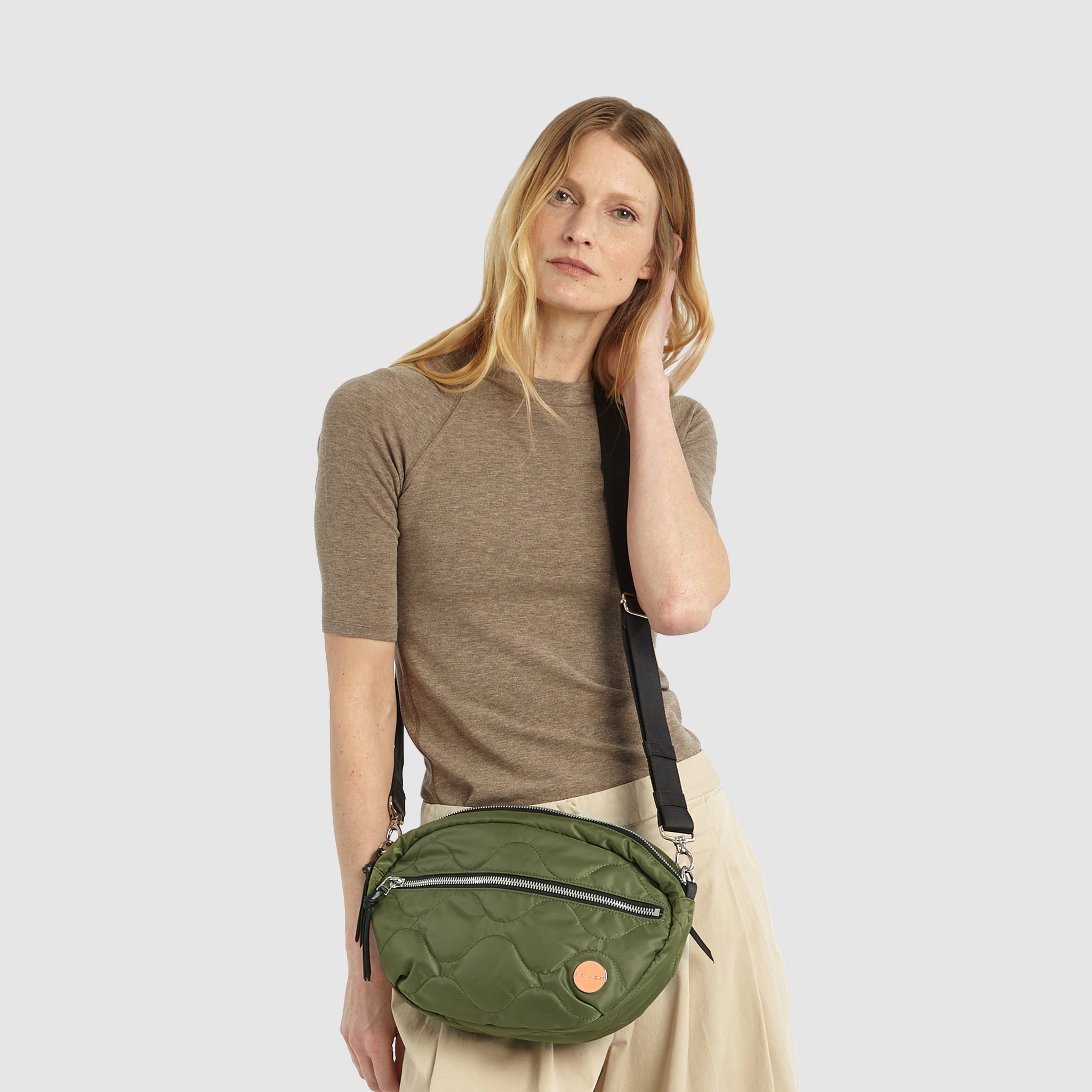 shortyLOVE cruiser medium crossbody bag in sage; on model in a tan top and pants against white background.