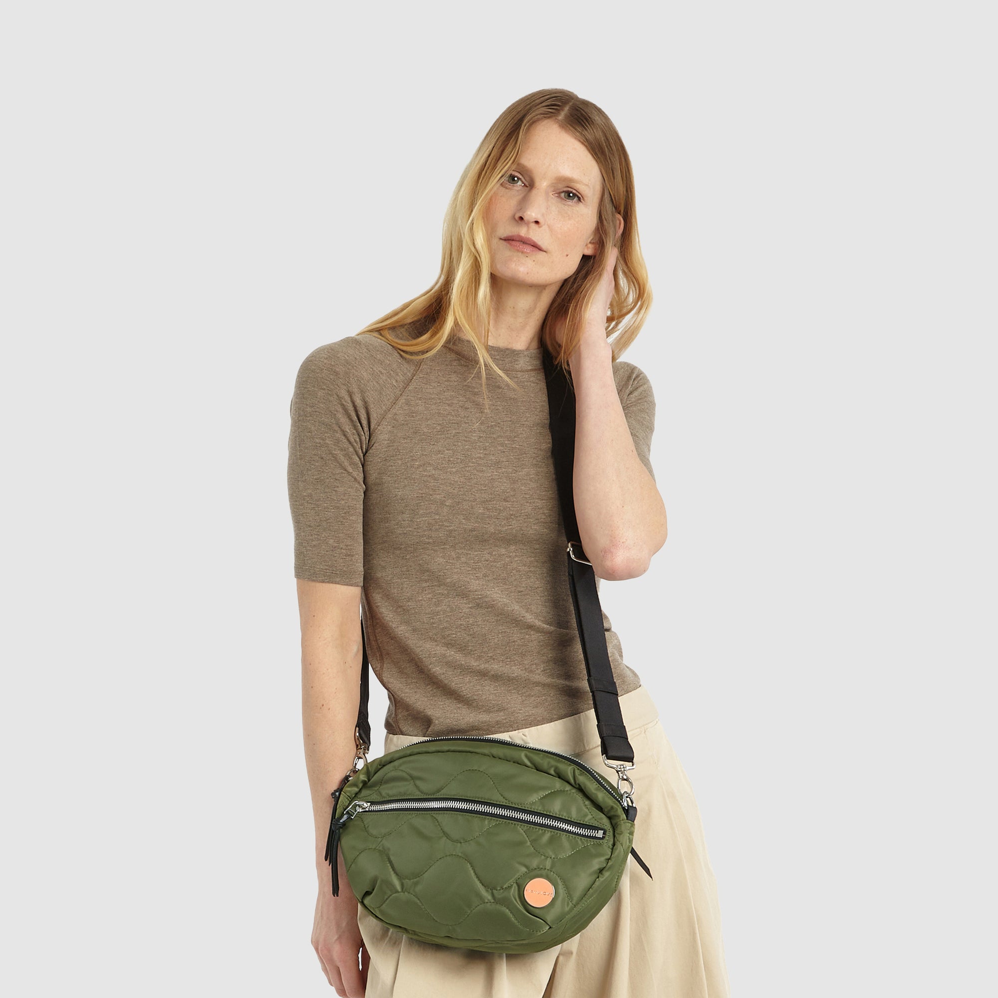 shortyLOVE cruiser medium crossbody bag in sage; on model in a tan top and pants against white background.