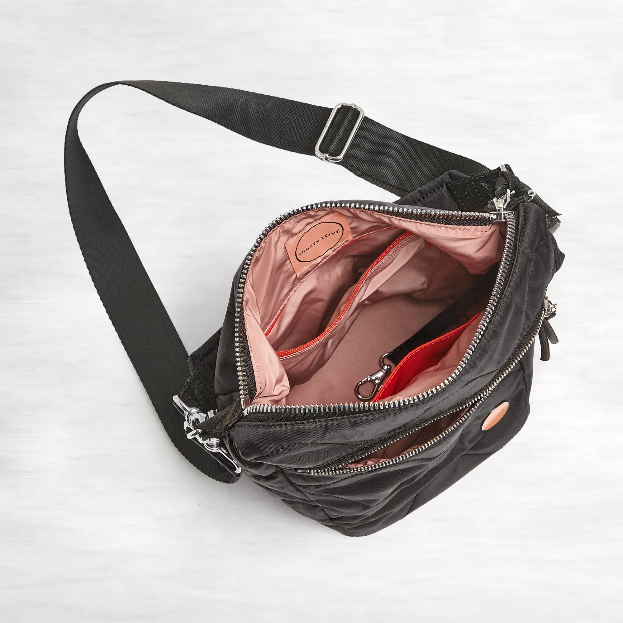 shortyLOVE marcel crossbody bucket bag in black; top-down view showing interior blush lining against white background.