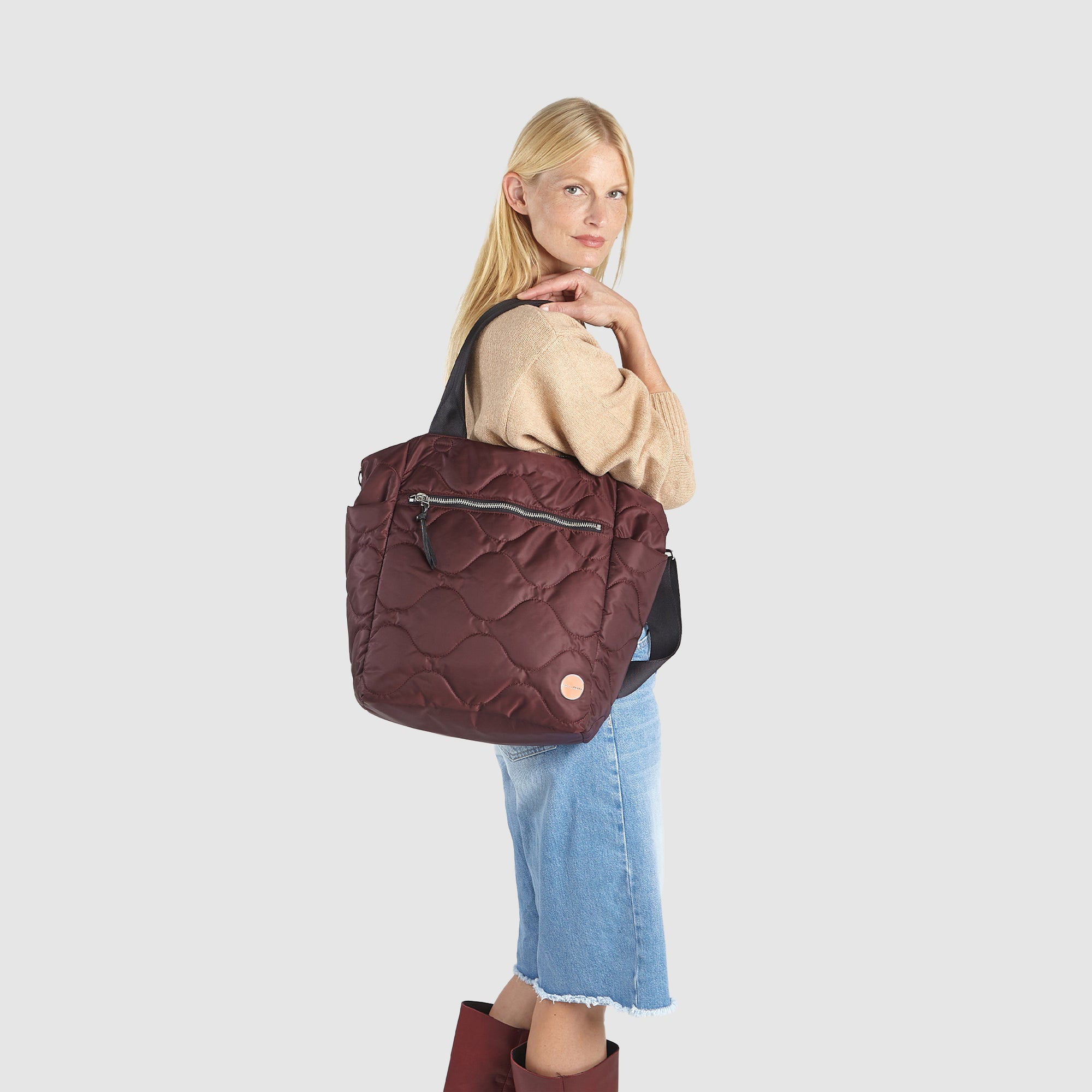 Woman wearing a maroon or bordeaux quilted ranger tote bag on a white background