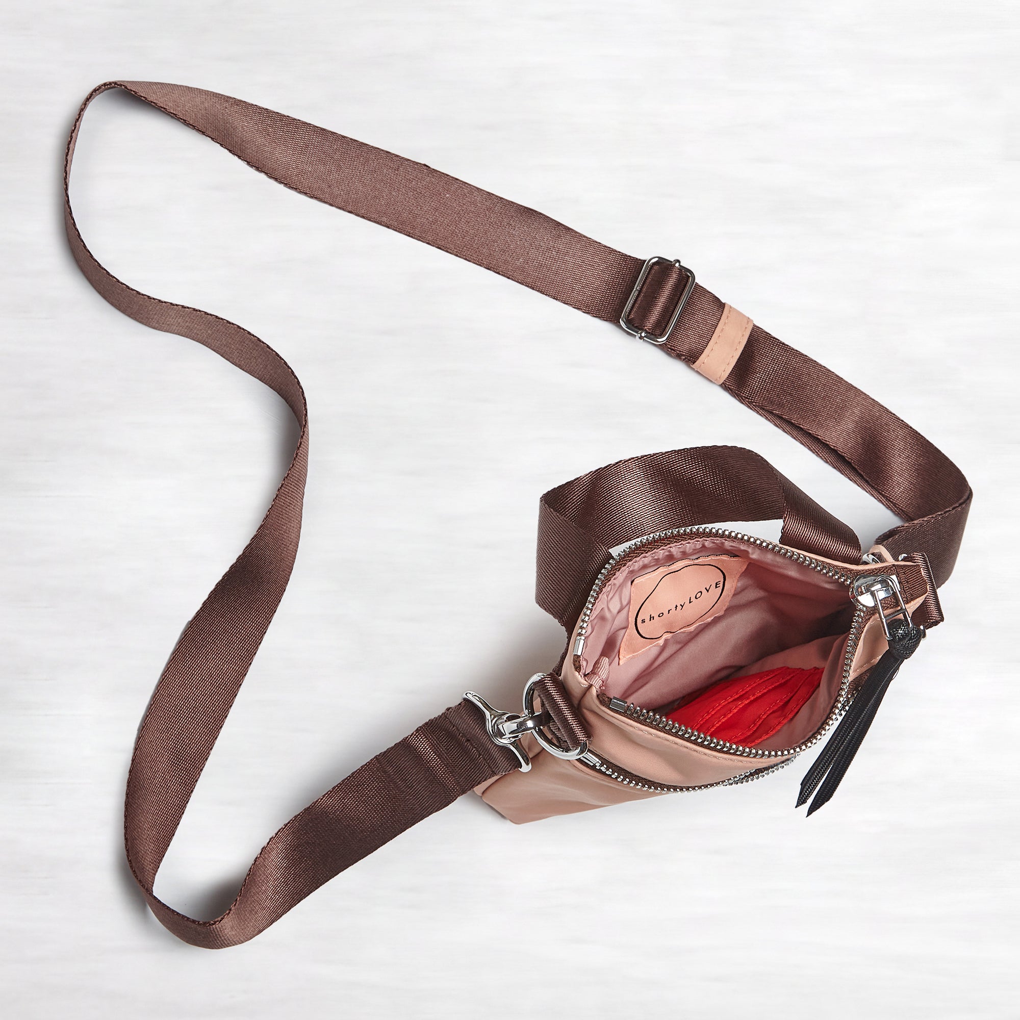 shortyLOVE shorthand small crossbody bag in dusty peach; top-down view showing interior blush/red lining against white background.