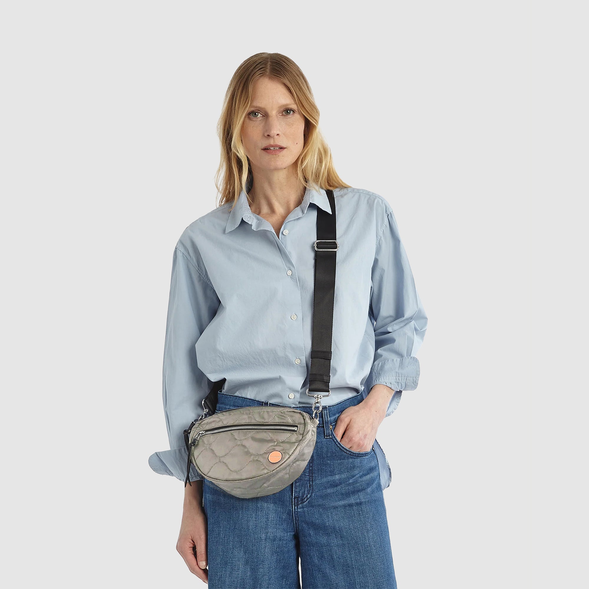 shortyLOVE small cruiser small crossbody bag in milky grey; on model in blue shirt and jeans against white background.